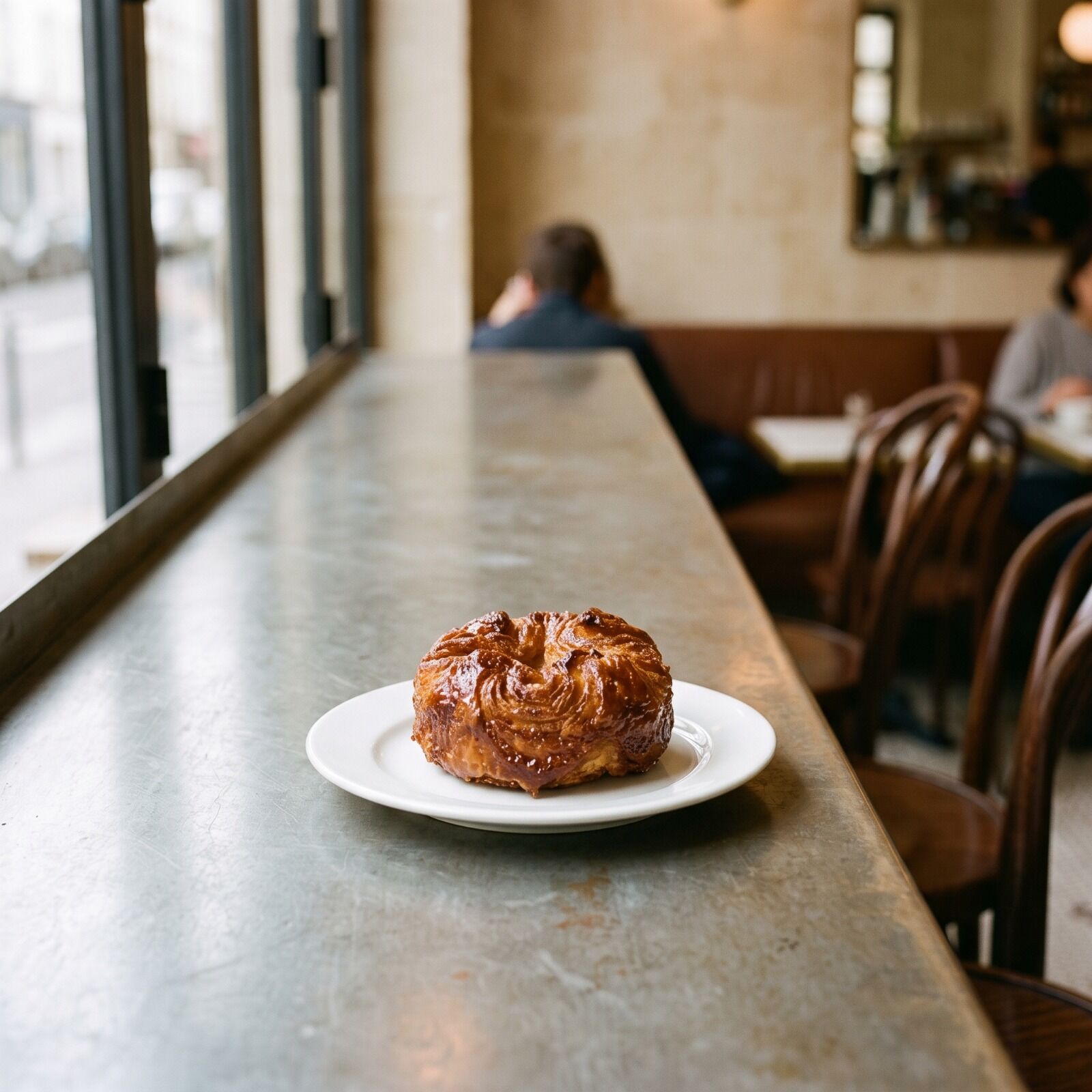 A caramelised kouign-amann on a plate, its layers lifting at the edge